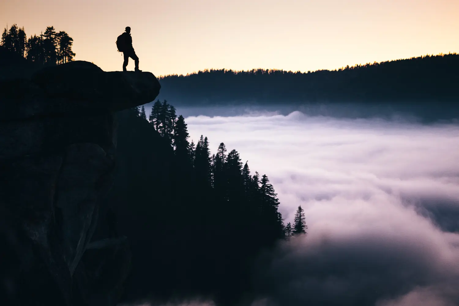 man standing in mountain overlooking trees at daytime